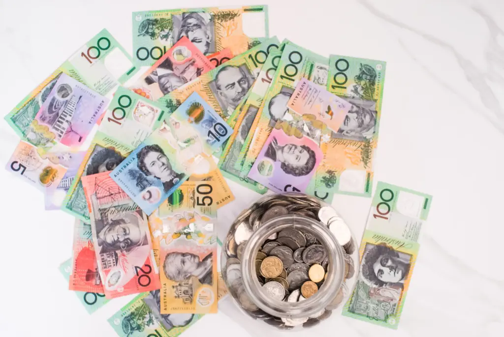 Australian bank notes spread on a marble-look surface with a jar of coins off-centre.