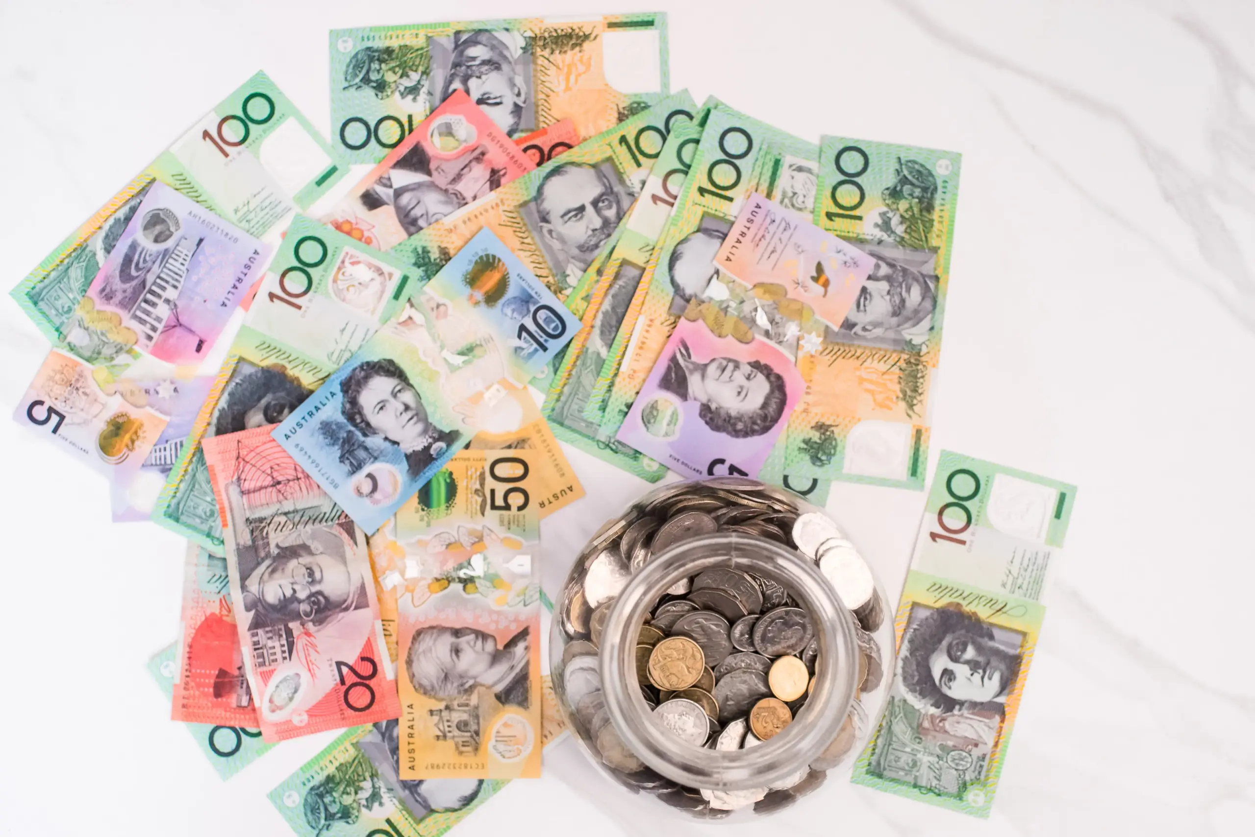 Australian bank notes spread on a marble-look surface with a jar of coins off-centre.
